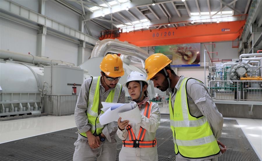 Three construction workers reviewing plans indoors, wearing safety gear.