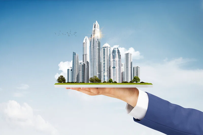 A hand holding a miniature city skyline against a clear sky.